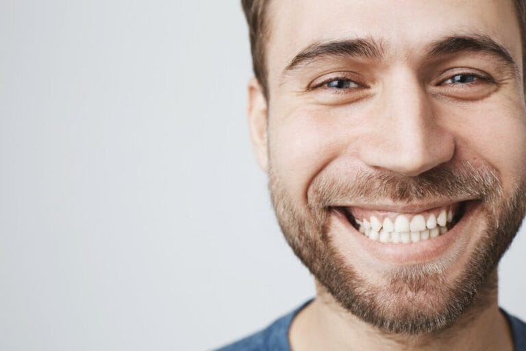 Close-up portrait of caucasian male model joyfully smiling with white perfect teeth. Good-looking happy carefree guy with stubble expressing positive emotions and feelings
